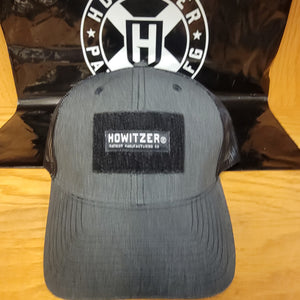 A black Howitzer branded trucker hat with a velcro patch on the front, displayed on a flat surface.