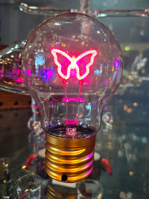 A neon light bulb with a butterfly , moon or star design illuminated in pink color, attached to a gold-colored base.