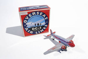 A toy model of a DC3 aircraft in silver and red colors, next to its packaging which has 'Overseas Airlines DC3' text.