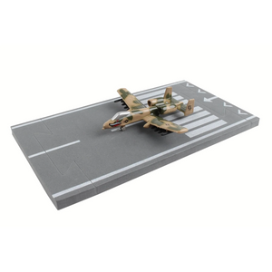 A miniature toy model of an A-10 Warthog aircraft in a desert camouflage pattern, displayed on a gray foam airplane runway base against a plain white background.