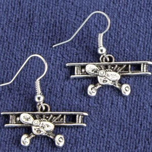 Silver airplane-shaped earrings on a blue fabric background