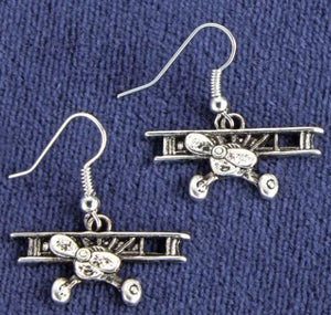 Silver airplane-shaped earrings on a blue fabric background