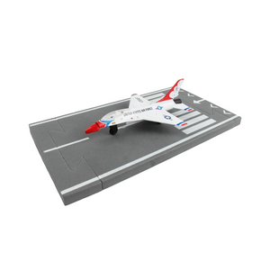 A small model United States Air Force jet airplane displayed on a gray runway base with white markings, photographed on a clean white background.