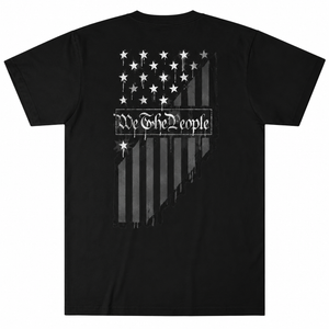 A black short-sleeve t-shirt with a distressed grayscale American flag graphic on the front, featuring the text 'We The People' in a gothic font across the center.