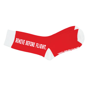 A pair of red socks with the text 'REMOVE BEFORE FLIGHT' written on the side, presented against a white background.