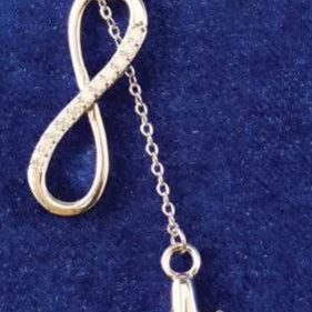 Silver airplane and infinity symbol necklace on a blue background