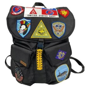Black backpack with various patches, including a United States Navy and Top Gun on a white background.