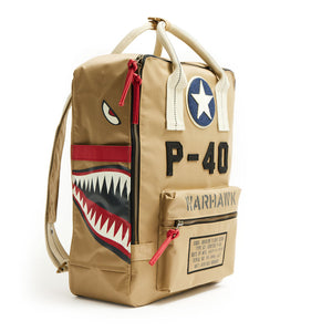 A beige nylon backpack featuring a vintage P-40 Warhawk logo with red and black accents, including a representation of a shark's mouth and teeth on the front pocket.