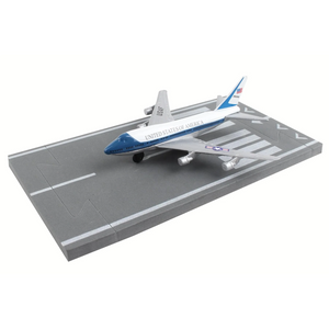 A scale model of a United States Air Force Lancer B-21 bomber aircraft displayed on a gray runway base with white markings, set against a plain white background.