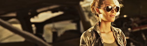 Woman wearing aviator sunglasses in a desert setting with aircraft in the background