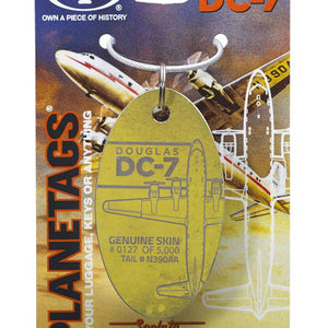 A gold-colored metal luggage tag with 'Douglas DC-7' text and an illustration of an aircraft behind it, mounted on a display card.