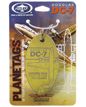 A gold-colored metal luggage tag with 'Douglas DC-7' text and an illustration of an aircraft behind it, mounted on a display card.