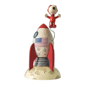 A figurine of Snoopy the astronaut, where Snoopy is depicted wearing a space suit and sitting in a rocket that is decorated with stars and an American flag.
