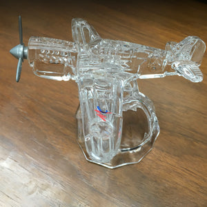 A clear glass paperweight in the shape of a vintage airplane, with visible details and a small American flag emblem.