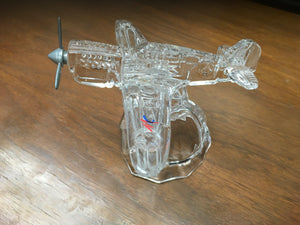 A clear glass paperweight in the shape of a vintage airplane, with visible details and a small American flag emblem.