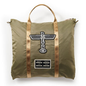 A green Boeing Totem helmet bag with felt applique totem patch, nylon webbing straps, and an antique brass YKK zipper.
