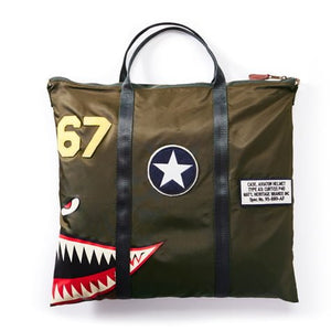 A green fabric helmet bag with a shark mouth design, star emblem, and text patches.