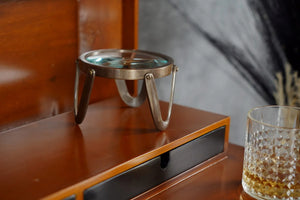 A brass desk magnifier with a glass base resting on a wooden surface.
