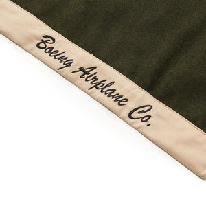A khaki-colored blanket with tan trim and the Boeing logo on the front, displaying the text 'BOEING AIRPLANE CO.'