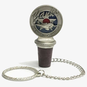 A pewter wine bottle stopper with a logo depicting a stylized airplane and 'Yanks Air Museum' on top, attached to a small chain.
