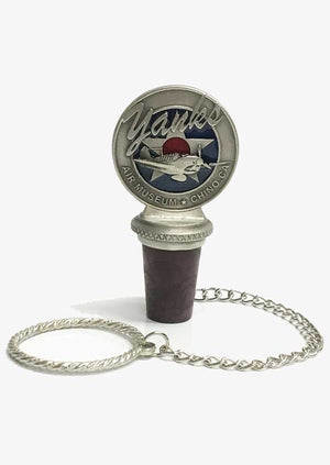 A pewter wine bottle stopper with a logo depicting a stylized airplane and 'Yanks Air Museum' on top, attached to a small chain.